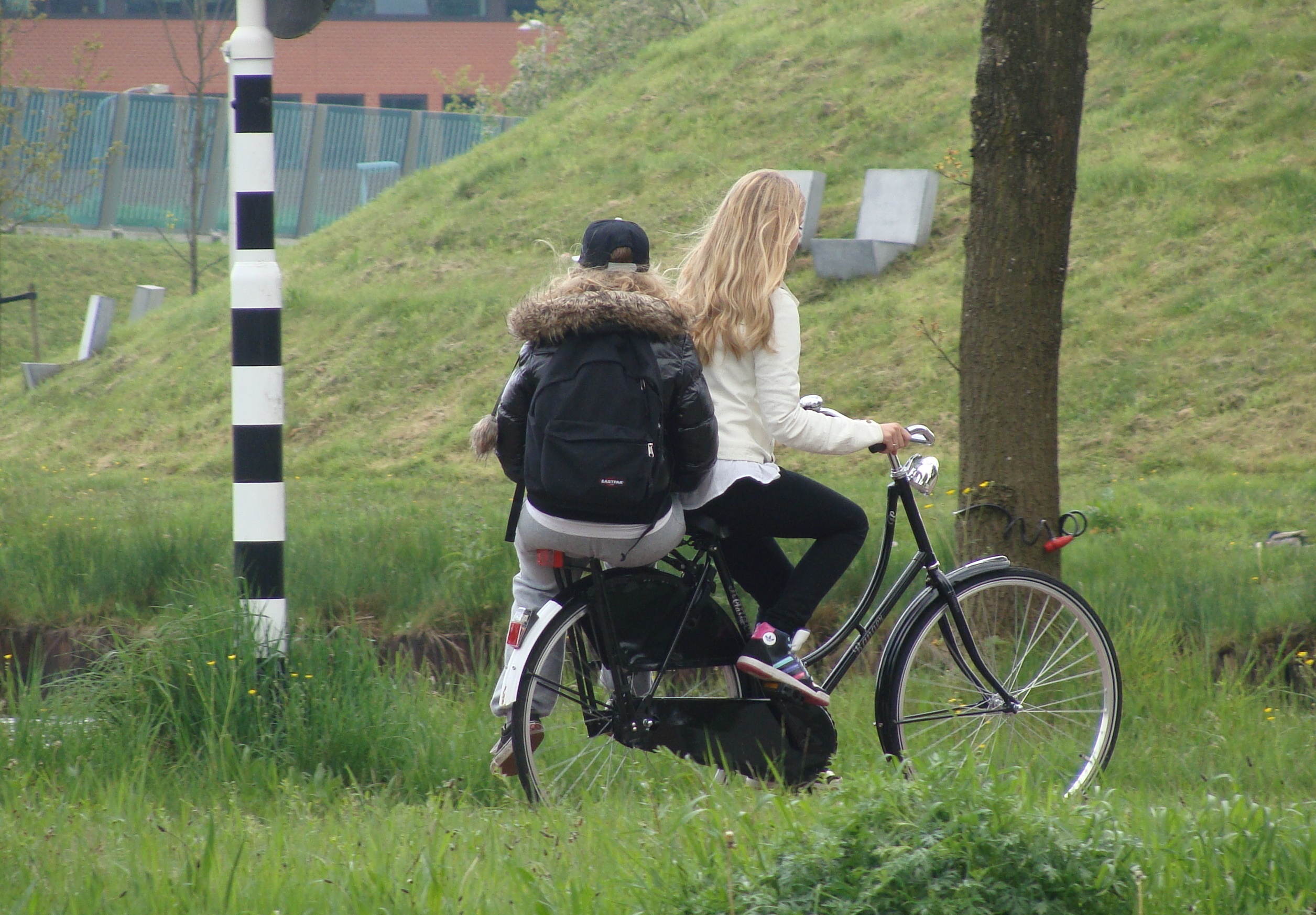 Two young people sharing one bike, one riding on the rear rack as the other pedals