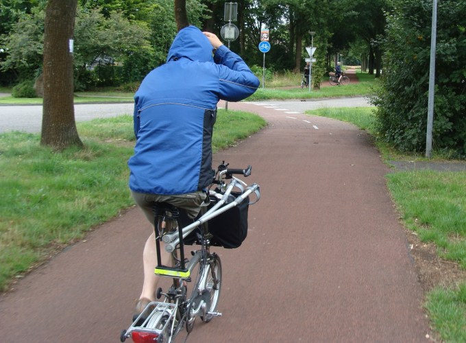 Cyclist on a wide red Dutch cycle path with a walking frame mounted on the front of the bike