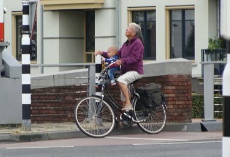 Older woman cycling with a toddler in a front child seat through a Dutch town