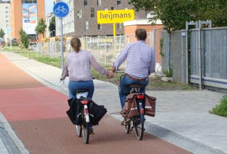 Couple cycling side by side holding hands on a red Dutch cycle path