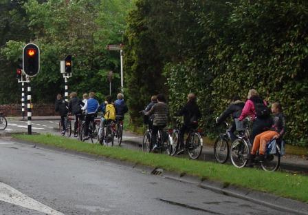 Children and teenagers on bikes waiting at a red traffic light on the school run