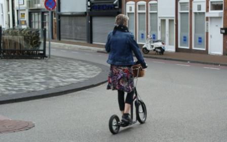 Woman riding a kick-scooter along a quiet Dutch town street