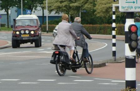 Older couple riding a tandem bicycle on a Dutch road past a junction
