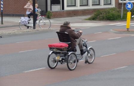 Older person riding an adult three-wheeled tricycle with a cushioned basket on a Dutch road