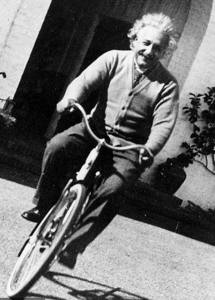 Albert Einstein smiling as he rides a bicycle in a garden, black-and-white photo