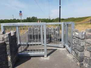 Galvanised steel V-shaped kissing gate set between stone walls at a greenway entrance