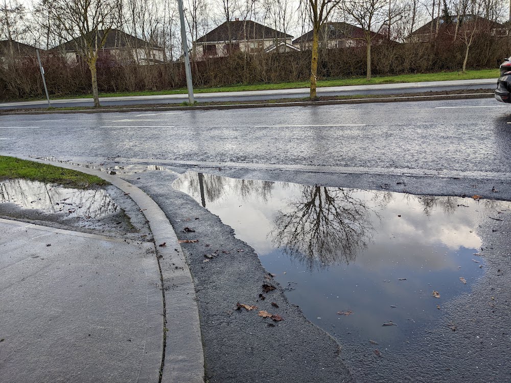 Large puddle flooding the cycle track at the entrance to Hayfield estate after rain