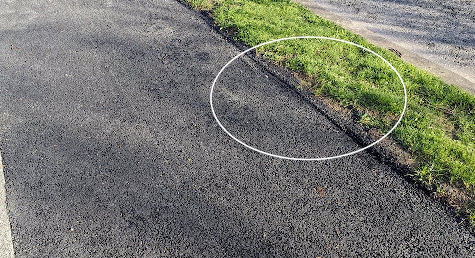 Close-up of the cycle track edge, ringed to show the missing kerb where asphalt crumbles into the grass verge