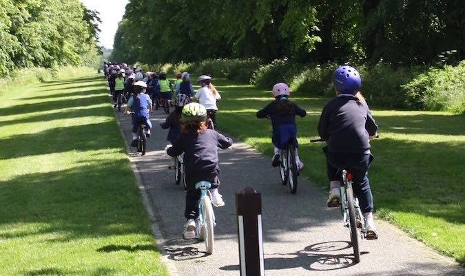 Schoolchildren in helmets cycling single file along the tree-lined Carton Walk path near Maynooth