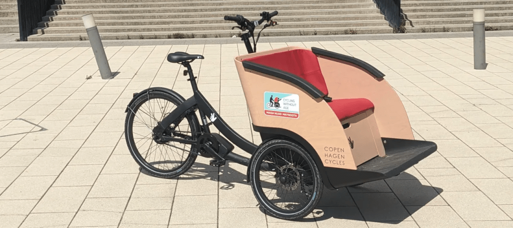 The campaign’s electric Cycling Without Age trishaw with its two-seat front passenger bench, parked on paving