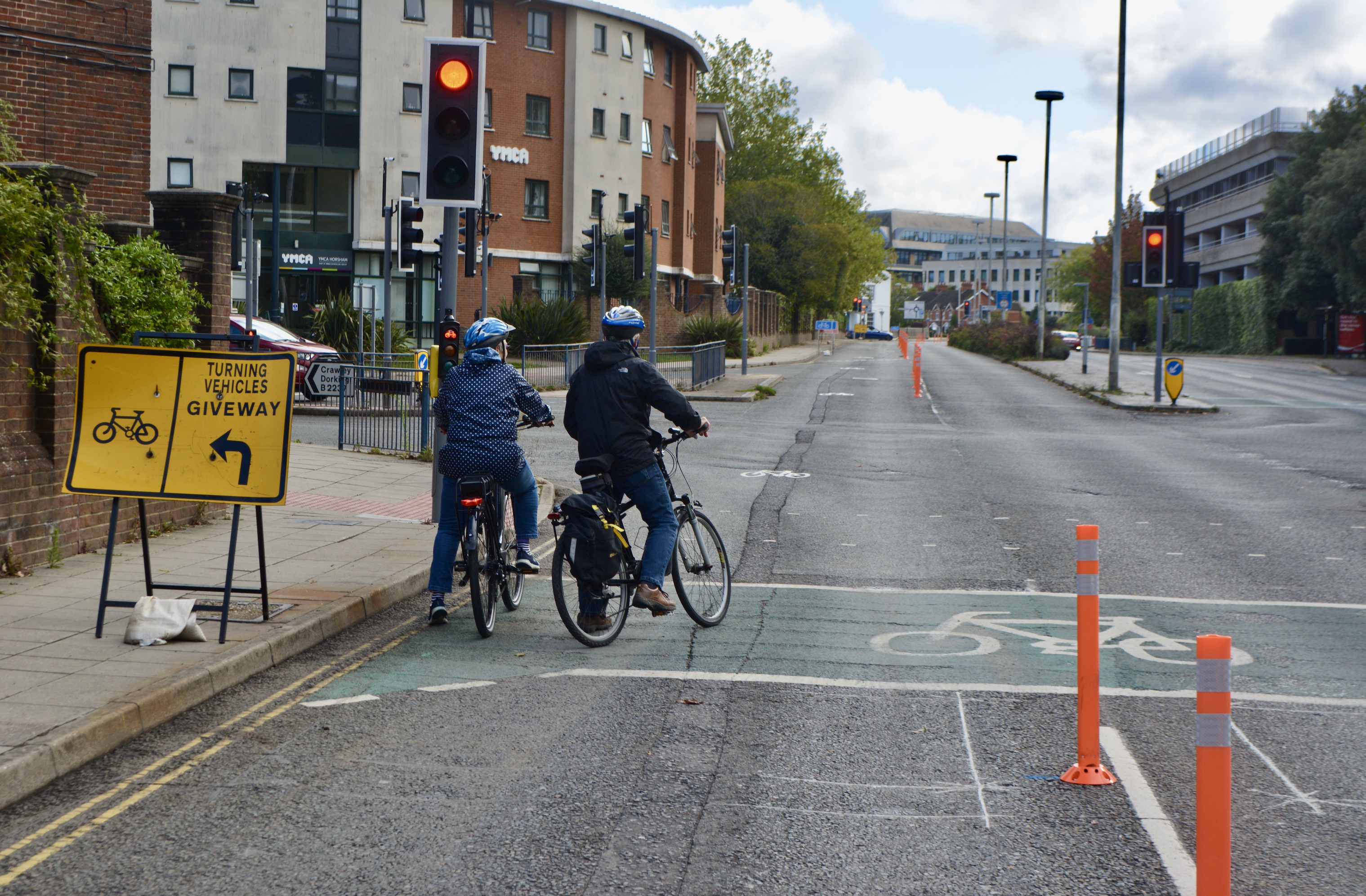 Two helmeted cyclists wait at a red light in a wand-protected pop-up cycle lane on Horsham’s Albion Way.
