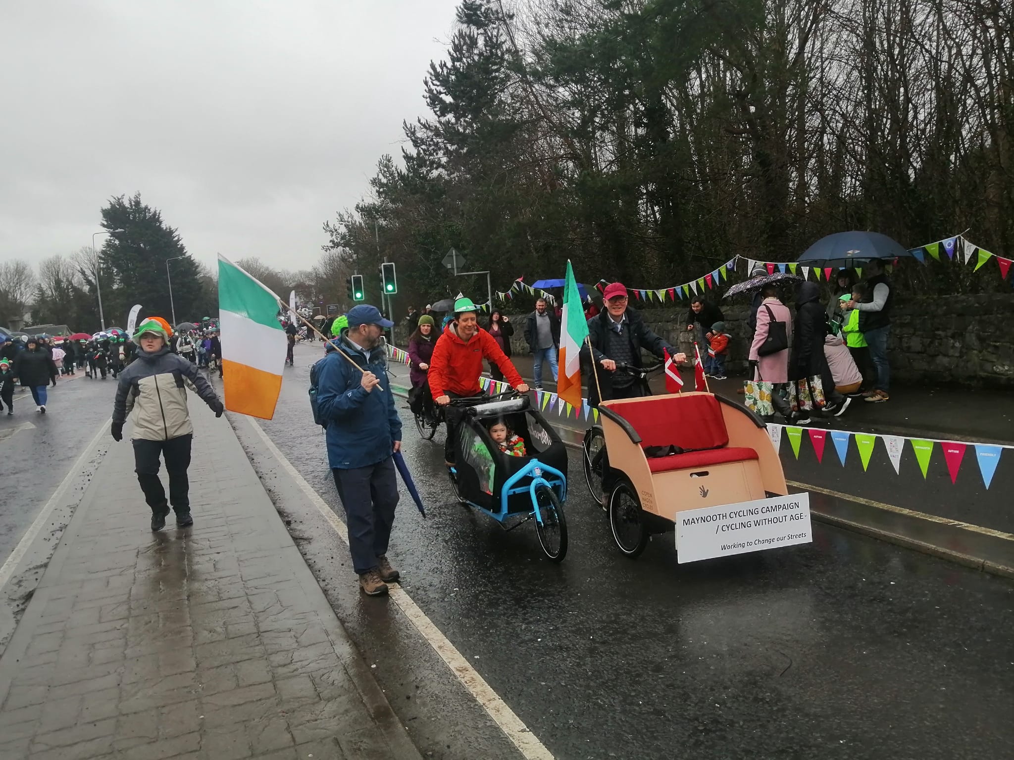 MCC members walk the rainy parade route with an Irish tricolour, a cargo bike and the bunting-decked trishaw