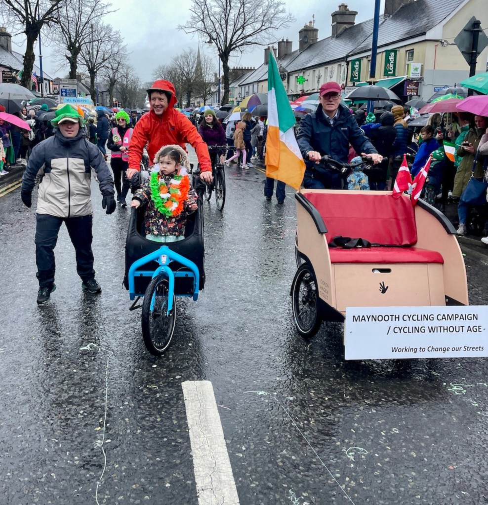 A child rides in the cargo bike beside the Cycling Without Age trishaw as the MCC group moves down the parade
