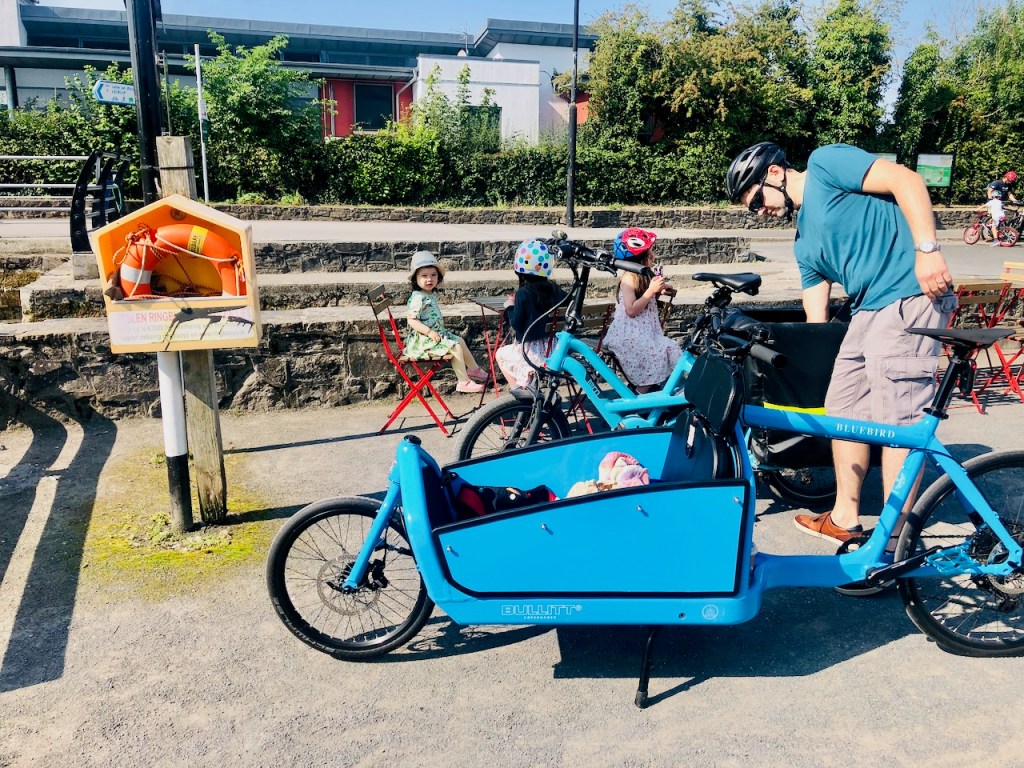 Parents and young children with two blue cargo bikes parked at Maynooth Harbour on a sunny day