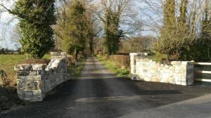 The greenway meets a public road at a stone-pillared crossing where trail users give way to road traffic.