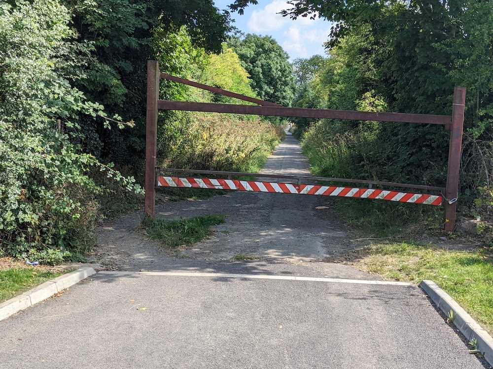 Rusted steel barrier with red-and-white chevrons blocking a tarmac path entrance near Limetree Hall, Maynooth